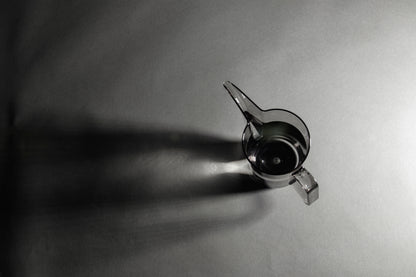 Transparent black plastic cup with handle and gooseneck style pour spout with water inside on a black and white background.