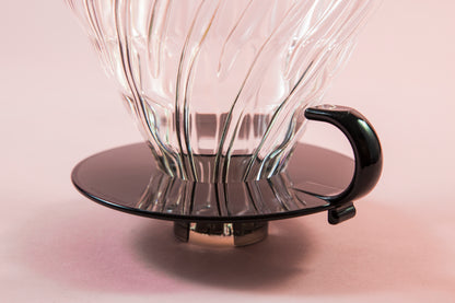 Close up of base on a clear glass cone shaped dripper with round black plastic base and handle.