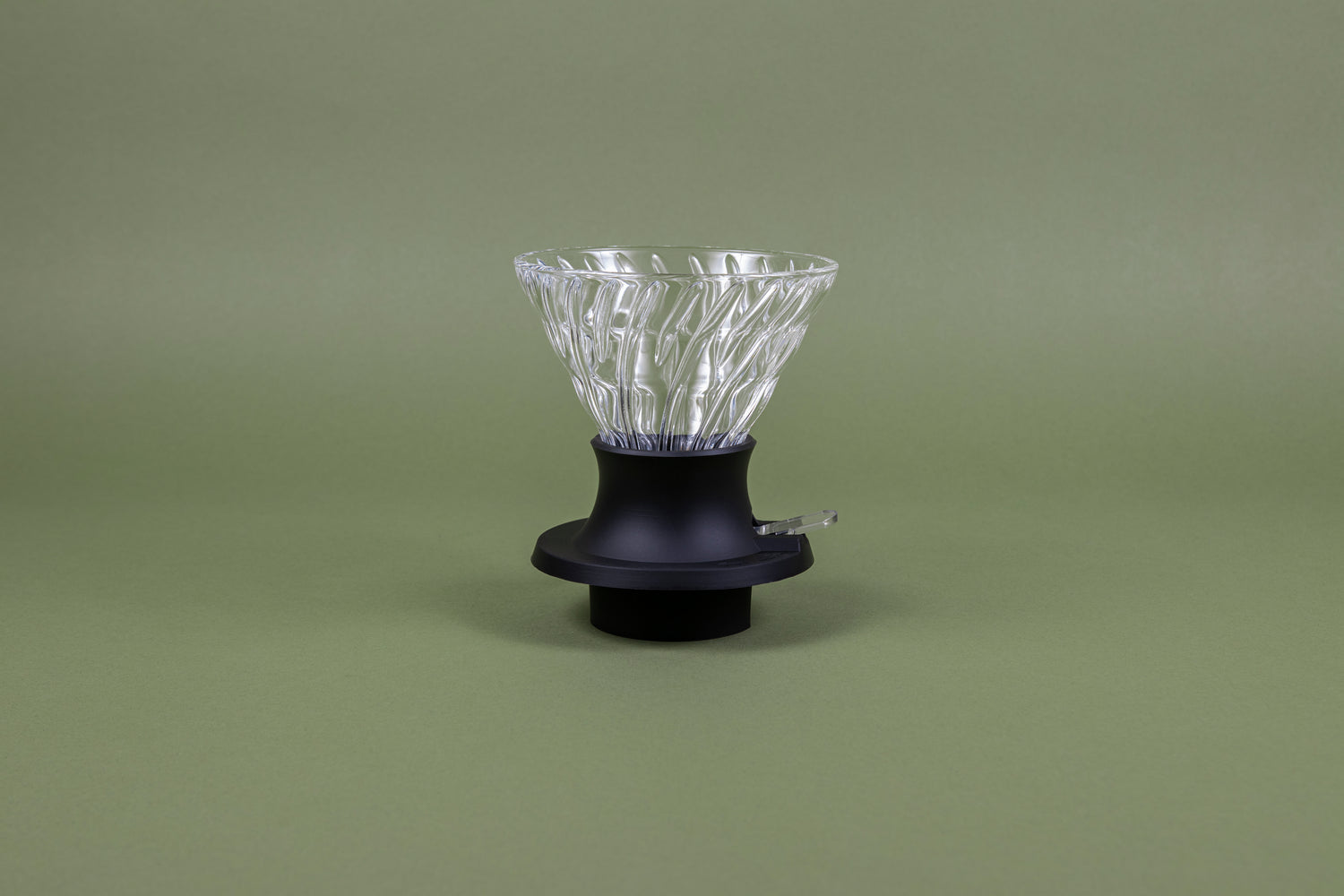 Cone-shaped glass dripper seated in a black plastic silicone base with clear plastic push switch on a green background.