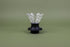 Cone-shaped glass dripper seated in a black plastic silicone base with clear plastic push switch on a green background.