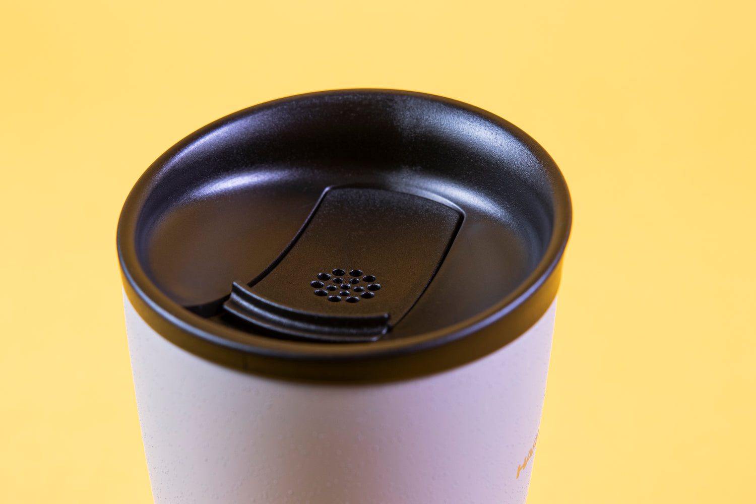 Close up of sloped black lid and sliding stopper with breathing holes on a textured white tumbler with Hario logo.