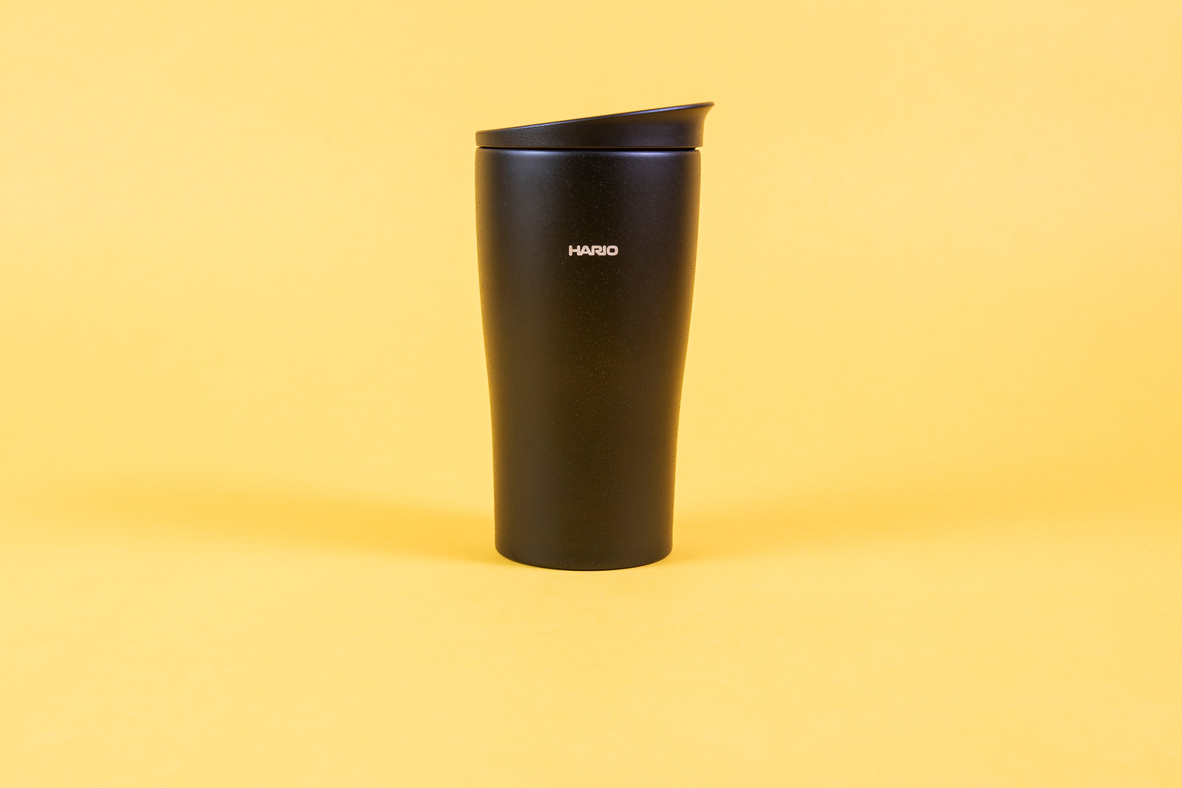 Textured black coffee tumbler with white Hario logo and black lid.
