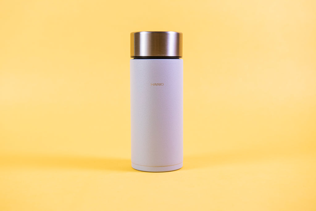 Slim cylindrical textured grey insulated cup with stainless steel lid set against a yellow background.