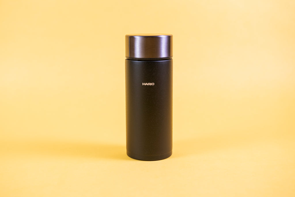 Slim cylindrical textured black insulated cup with stainless steel lid set against a yellow background.