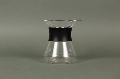 Hourglass shaped glass server with stainless steel wire dripper and black silicone rubber band.