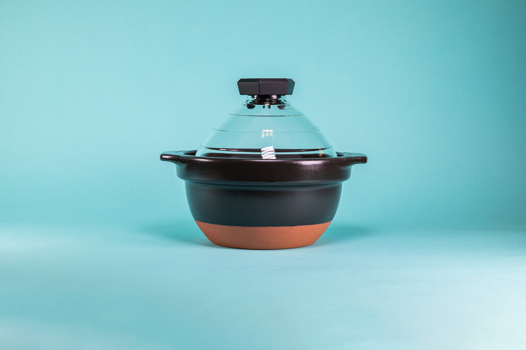Black ceramic rice cooker with clay-colored powder coated bottom, glass lid, and black plastic lid knob.