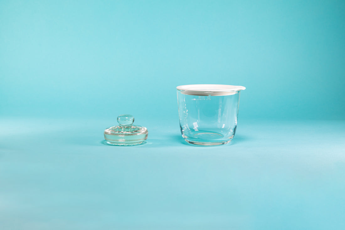 Small glass salting bowl with white silicone lid and weighted glass stone with glass knob for pickling and set against a blue background.