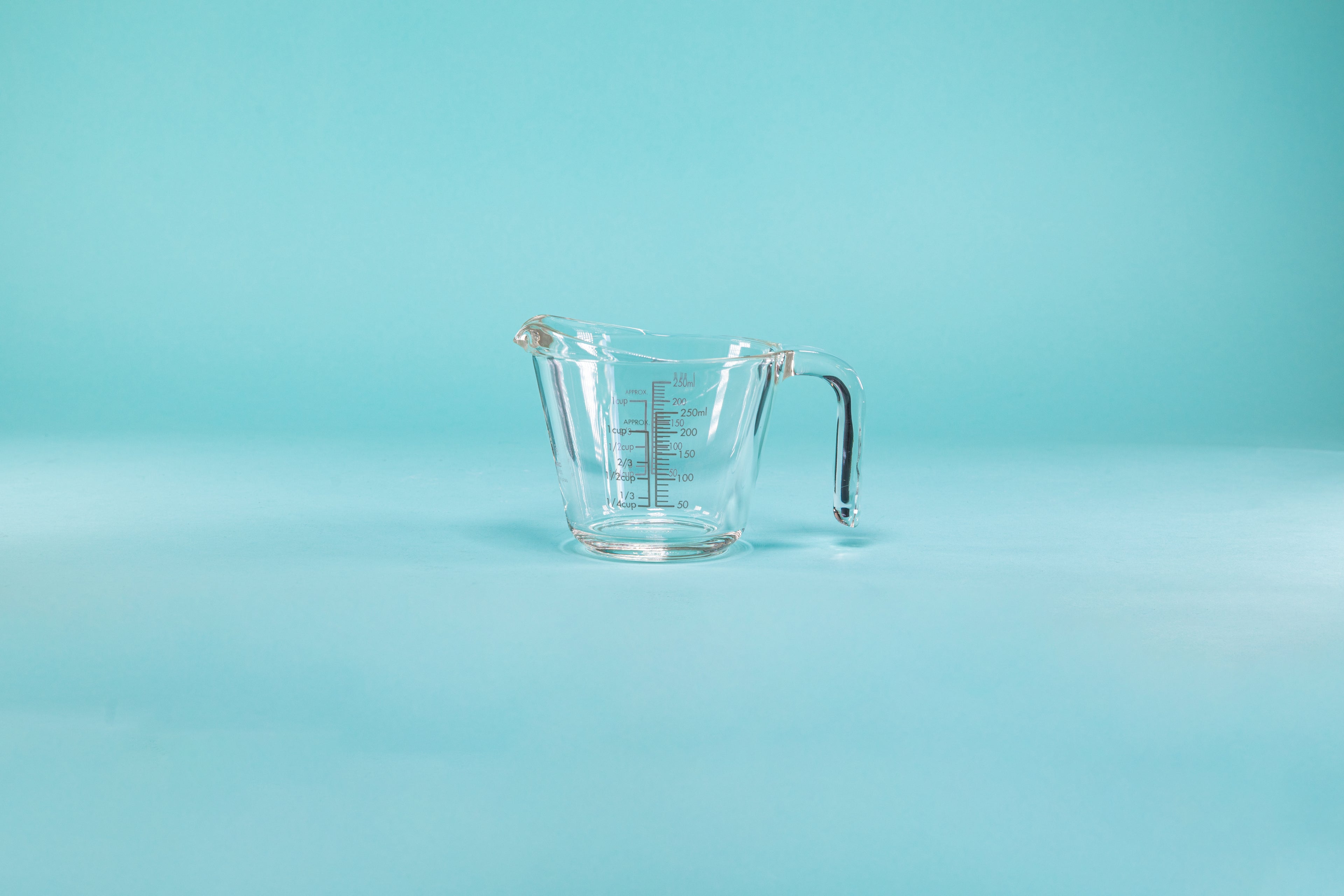 Thick glass measuring cup with glass handle and measurements on both the outside and inside of the glass.
