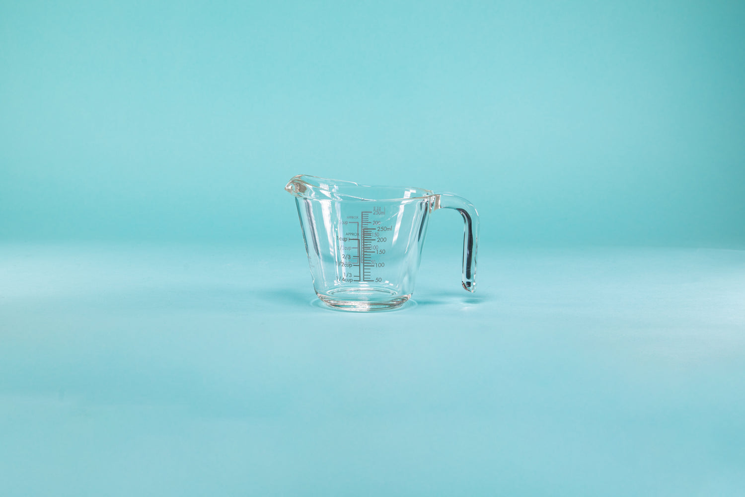 Thick glass measuring cup with glass handle and measurements on both the outside and inside of the glass.