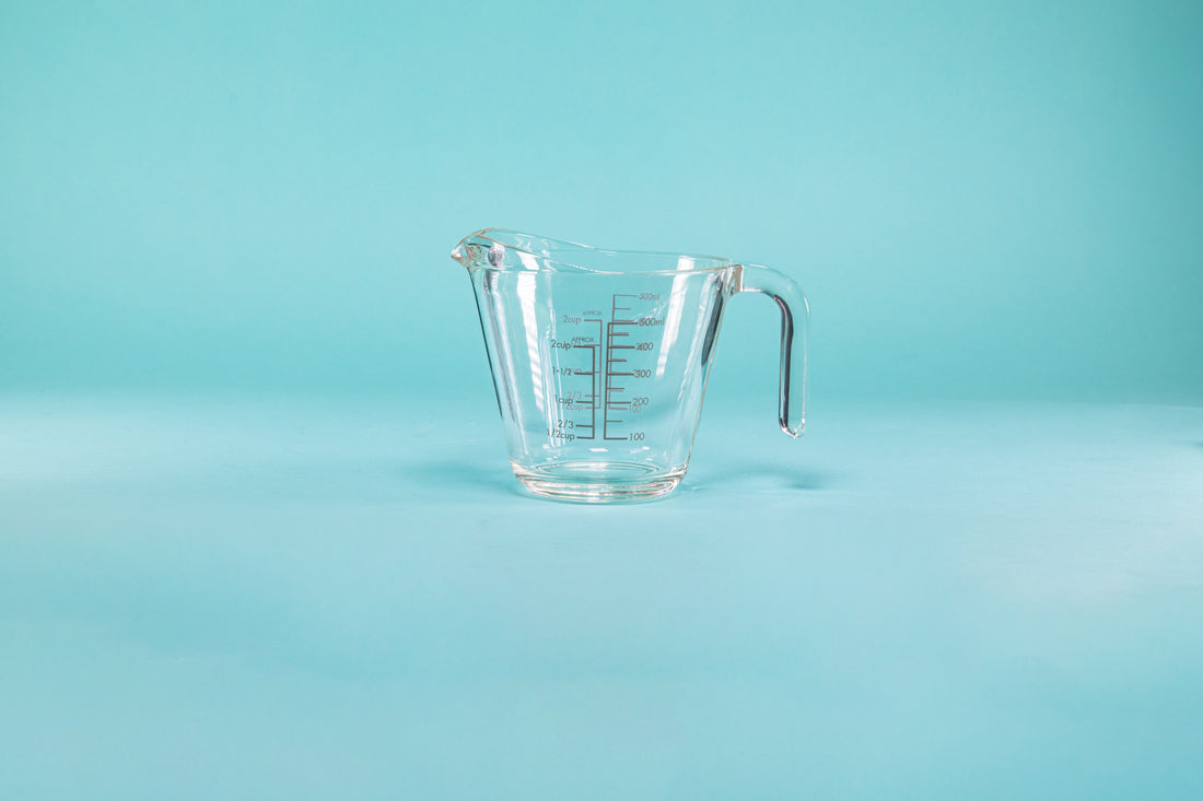 Thick glass measuring cup with glass handle and measurements on both the outside and inside of the glass.