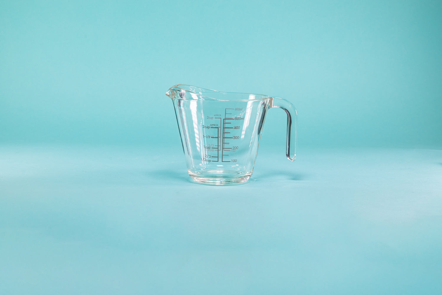 Thick glass measuring cup with glass handle and measurements on both the outside and inside of the glass.