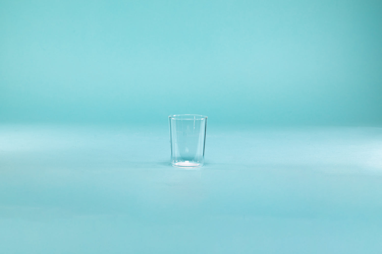 Clear thin walled shot glass on blue background.