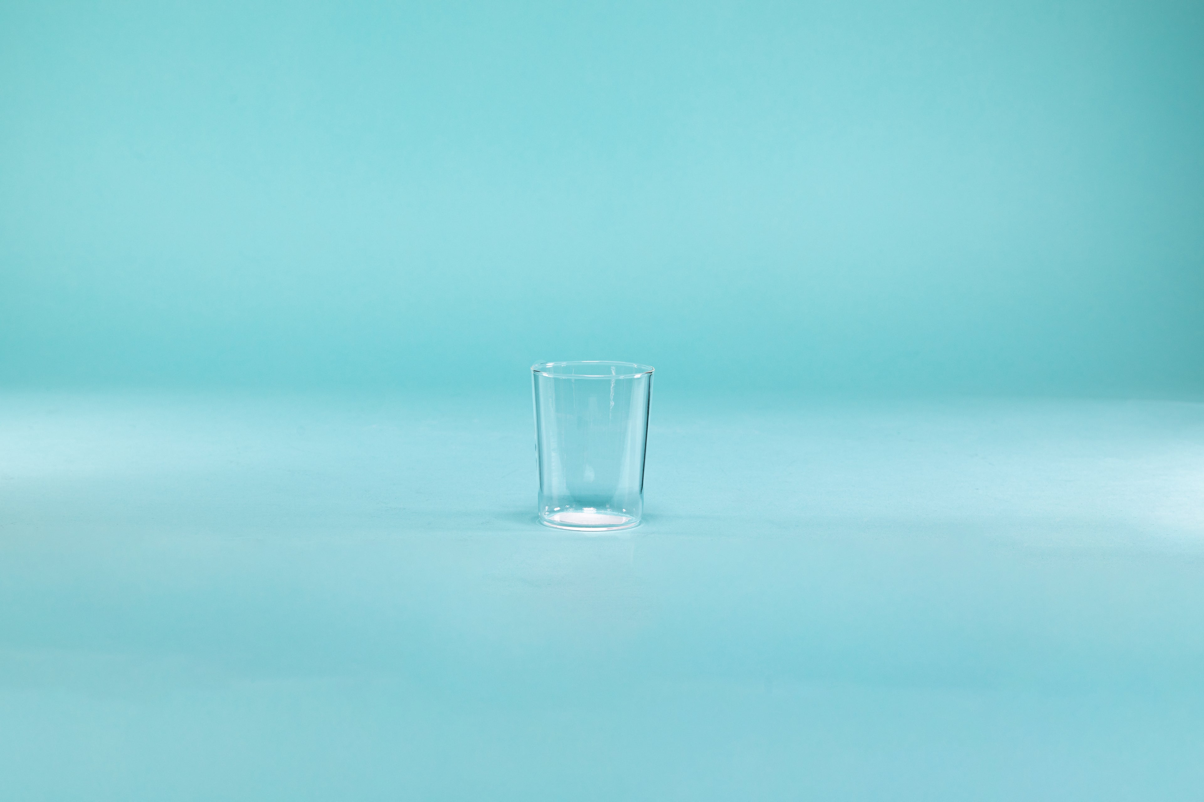 Clear thin walled shot glass on blue background.