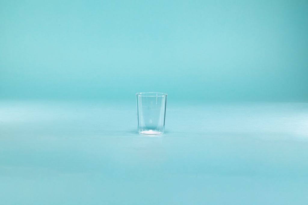 Clear thin walled shot glass on blue background.