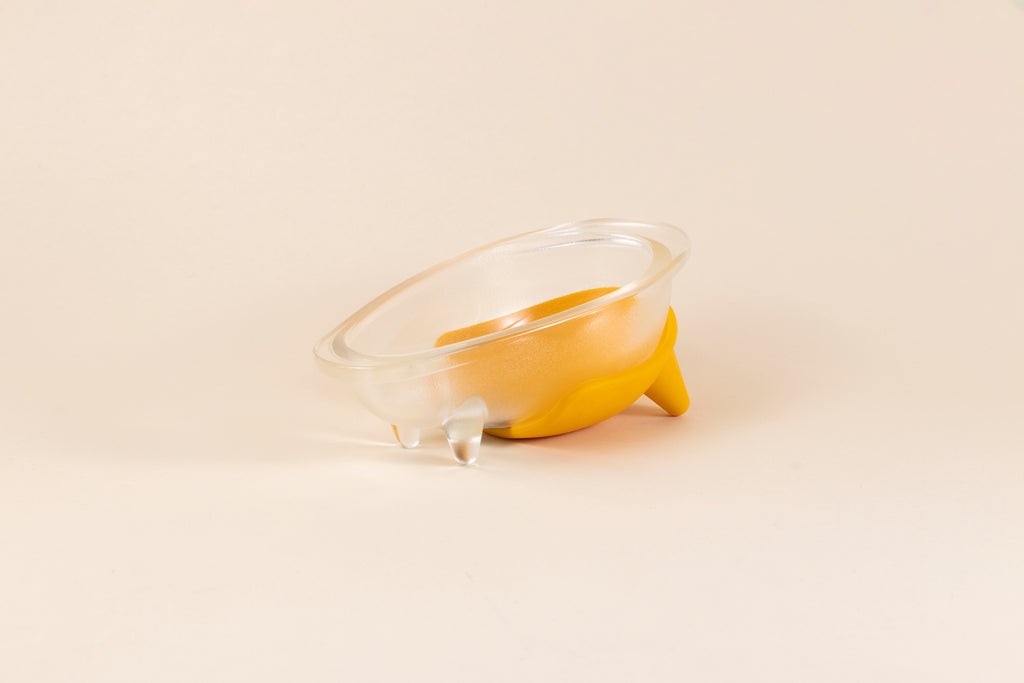 Glass dog bowl shaped like a bathtub with mango yellow silicone non-slip mat.