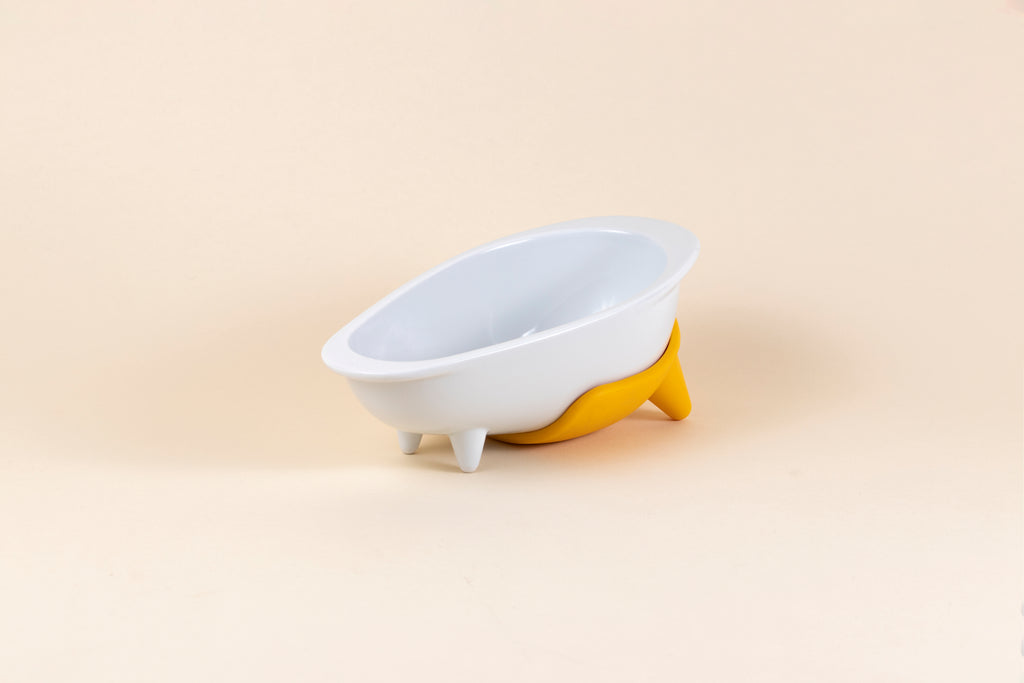 White glazed porcelain dog bowl shaped like a bathtub with mango yellow silicone non-slip mat.