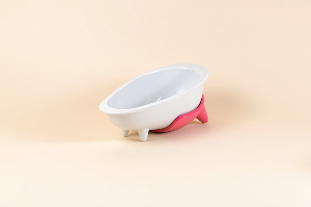 White glazed porcelain dog bowl shaped like a bathtub with pink silicone non-slip mat.
