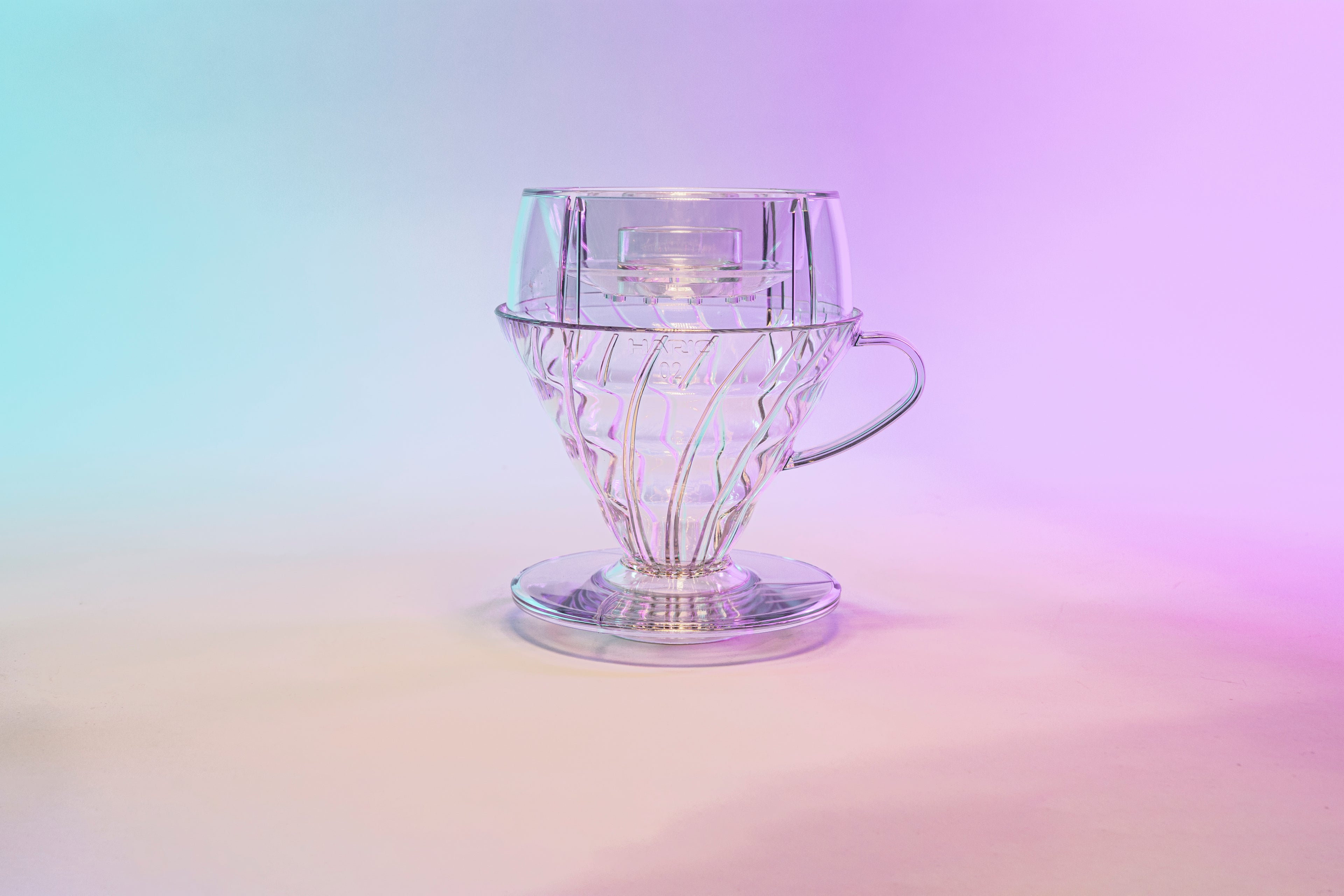 Clear plastic cone shaped dripper with clear plastic round drip assist seated on top and set against a blue and purple gradient background.