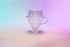 Clear plastic cone shaped dripper with clear plastic round drip assist seated on top and set against a blue and purple gradient background.