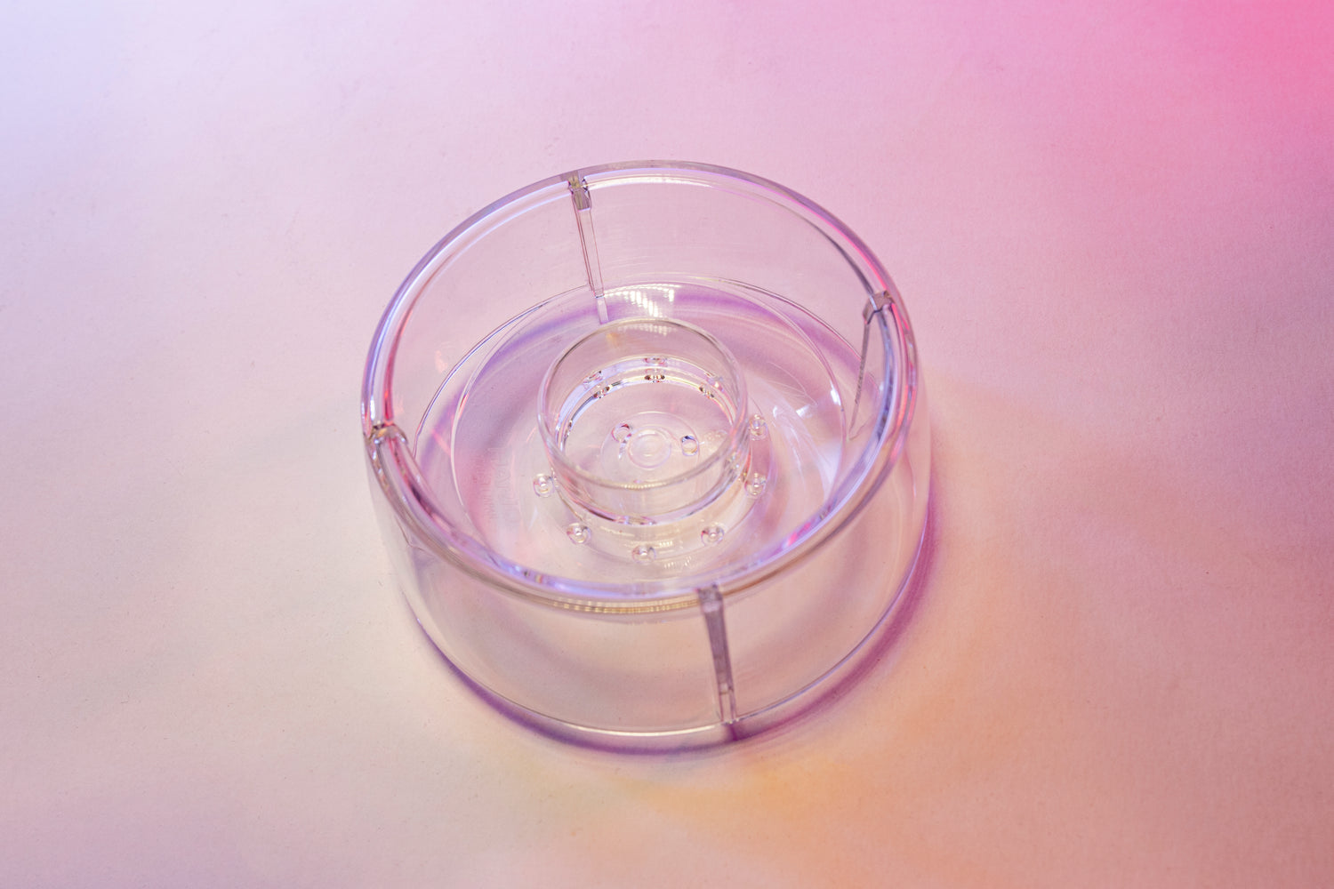 Clear plastic ring with interior smaller ring and holes for liquid to drain through. Set on a pink background.