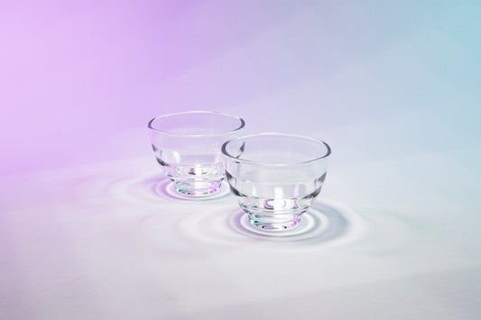Two matching short glass tea cups with beehive shape against purple to blue gradient background.