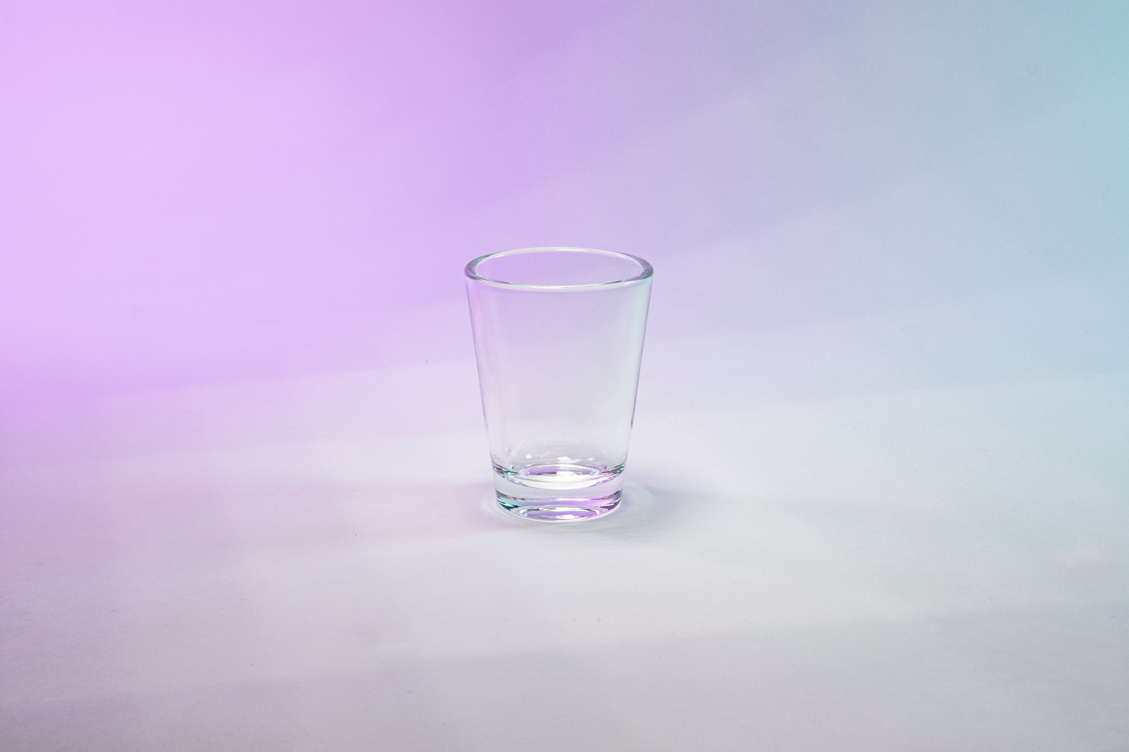 Clear shot glass against purple to blue gradient background.