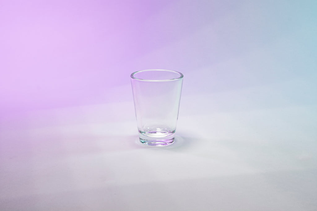 Clear shot glass against purple to blue gradient background.