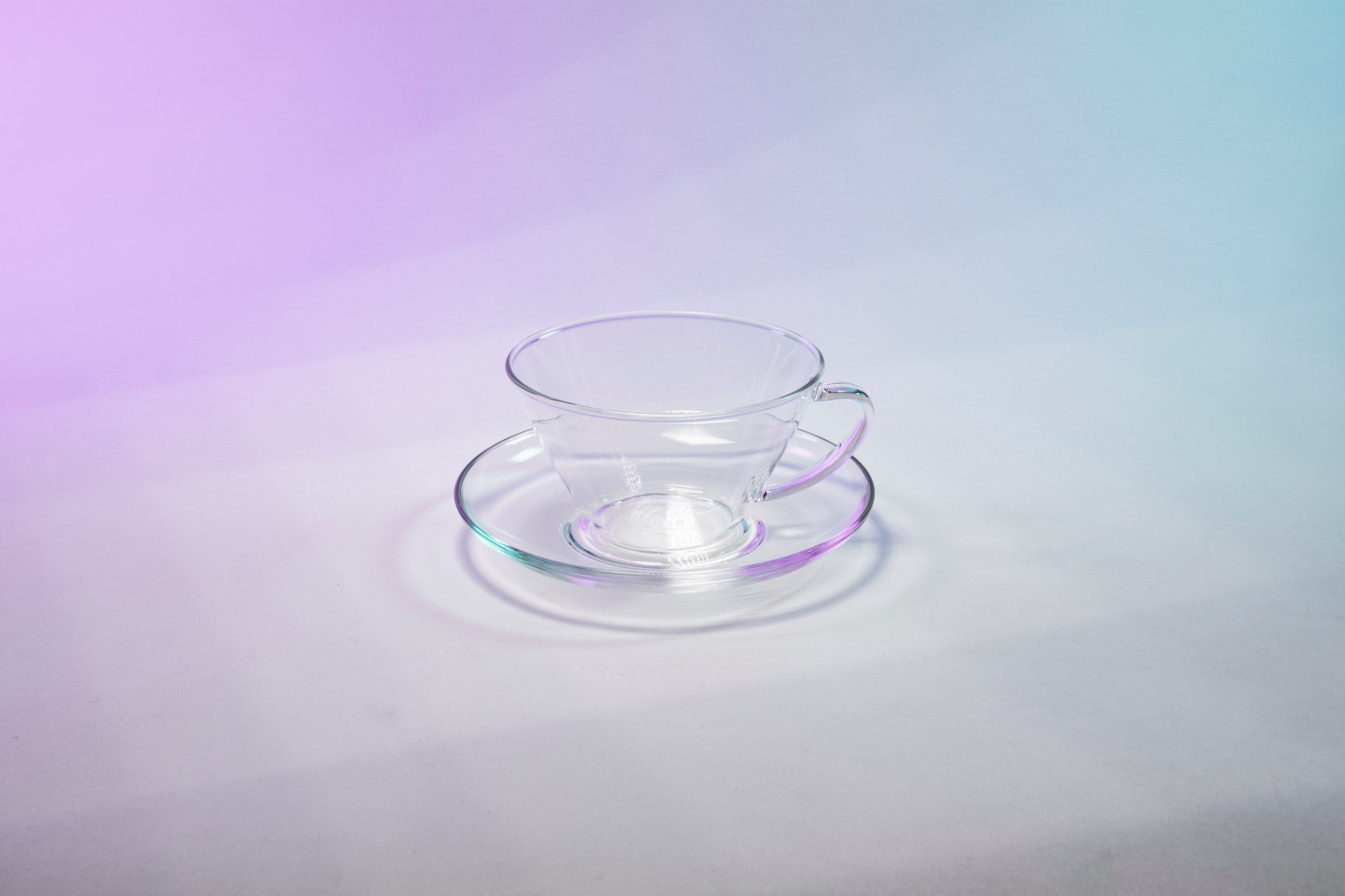 Tapered small glass cup with full glass handle sitting in a matching glass saucer.