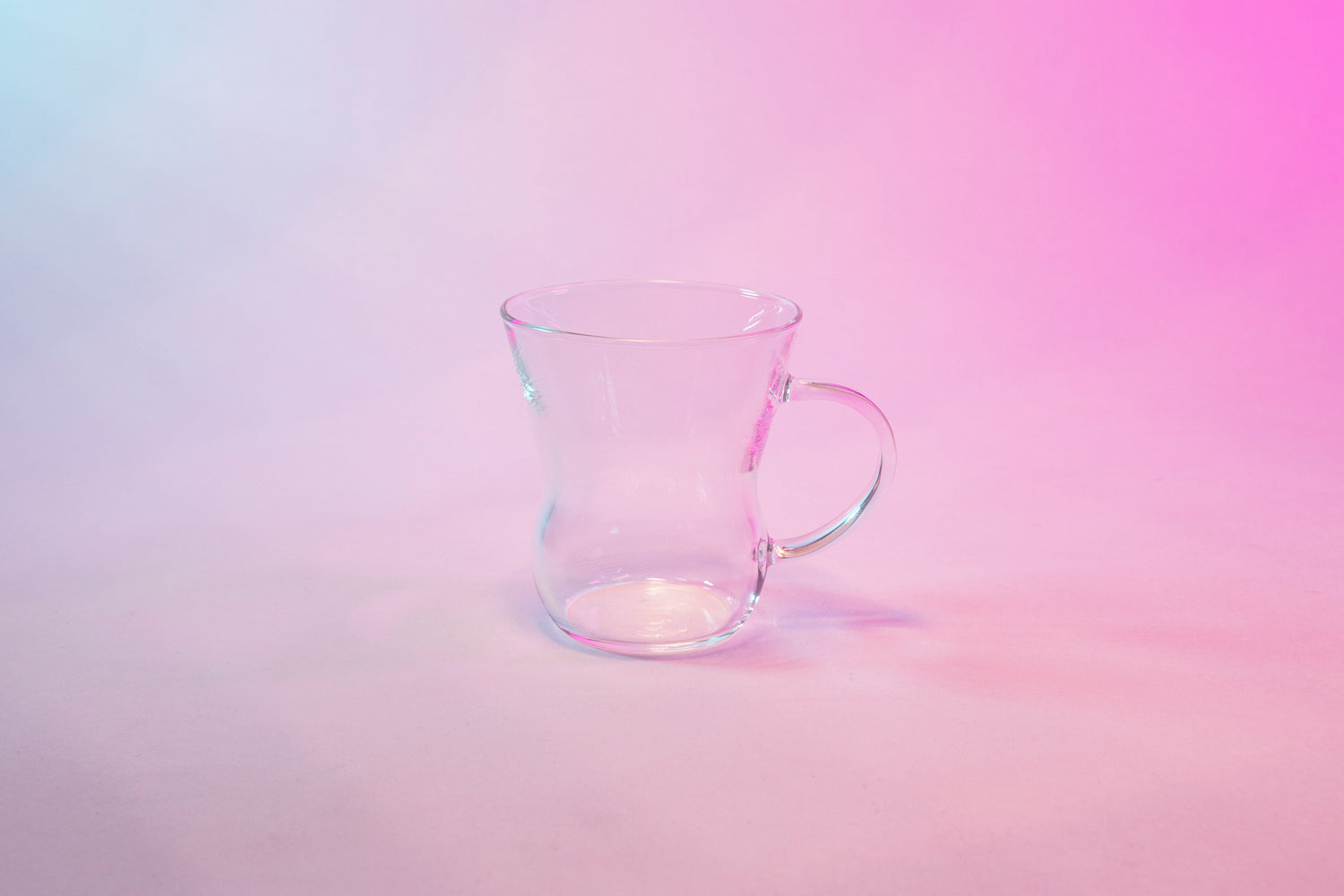 Clear glass tapered mug with full glass handle against a background with blue to violet gradient.