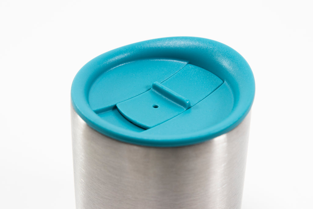 Close up of a light blue silicone lid showing sliding stopper and the top of a short stainless steel insulated mug.