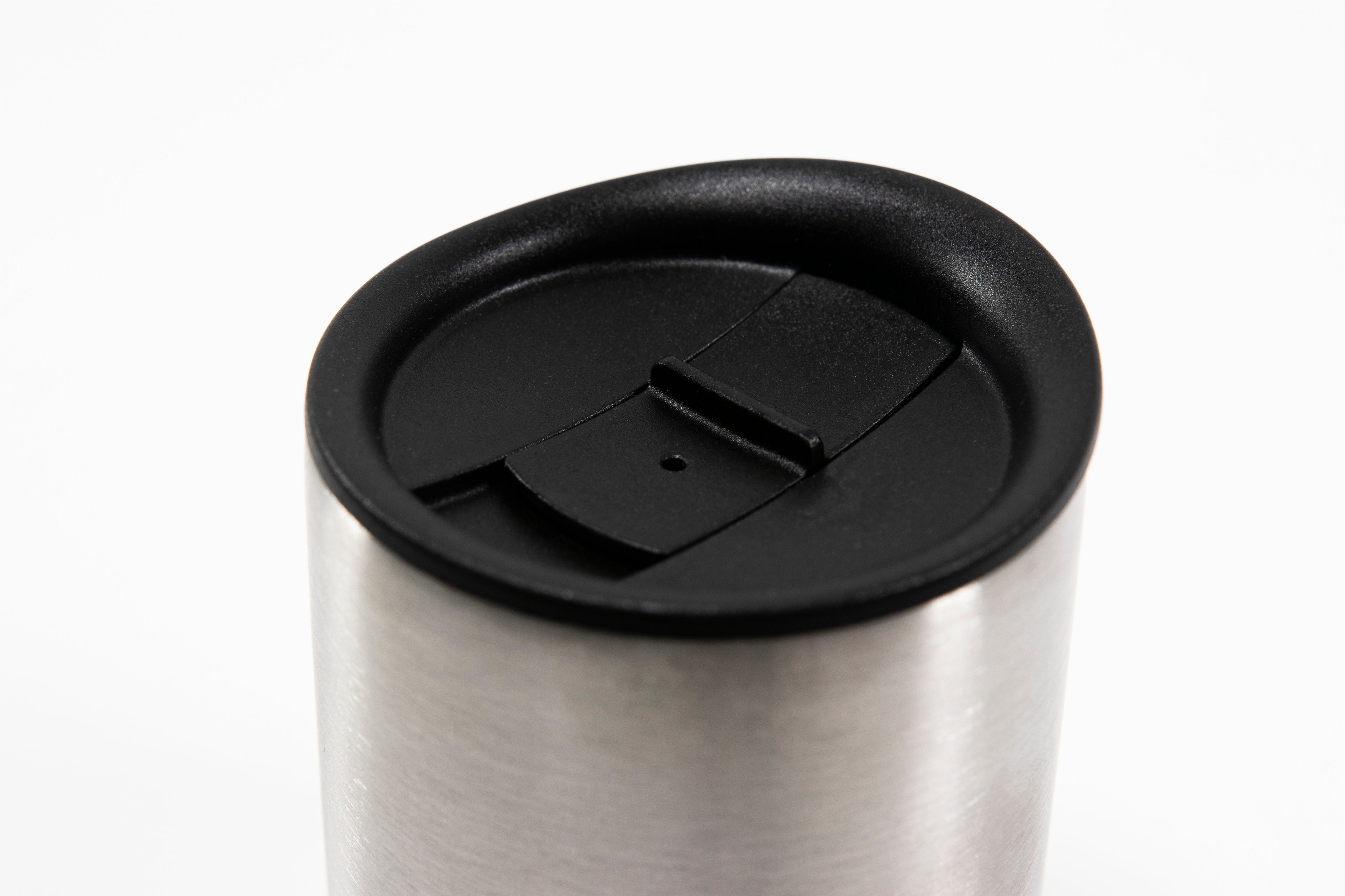 Close up of black silicone lid showing sliding stopper and the top of a short stainless steel insulated mug.