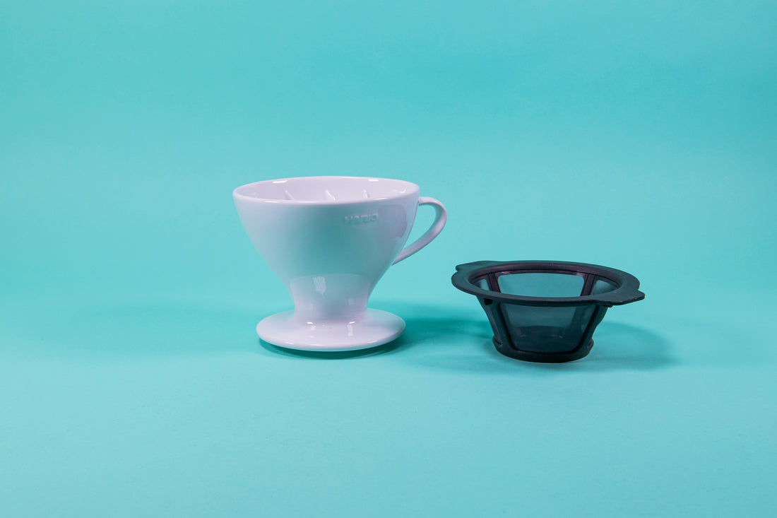 White ceramic cone shaped dripper with ridges inside, rounded eges, and black plastic filter insert seated next to it on a blue background.