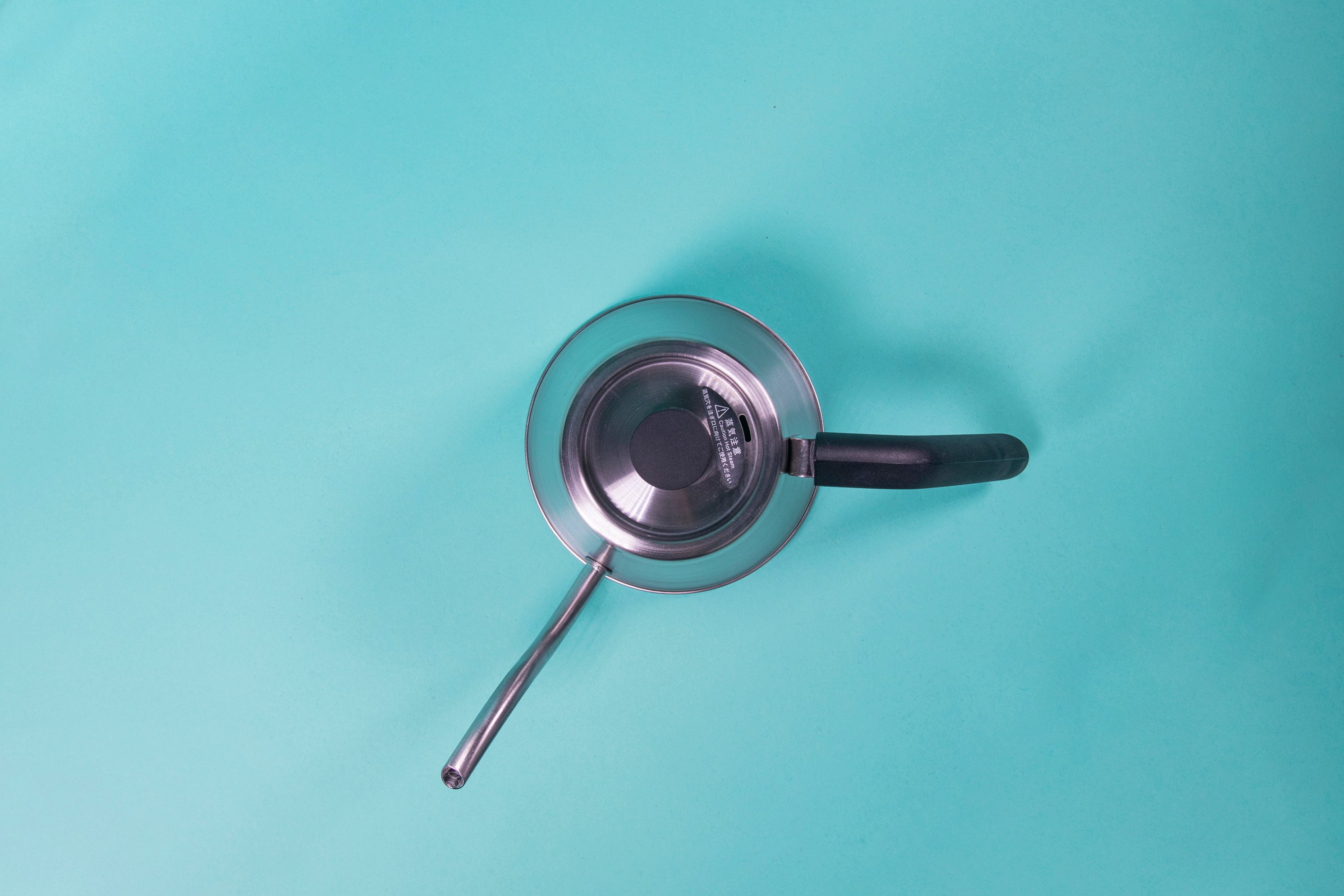Showing the top of a silver stainless steel kettle with black plastic handle and short cylindrical black plastic lid knob set against a blue background.