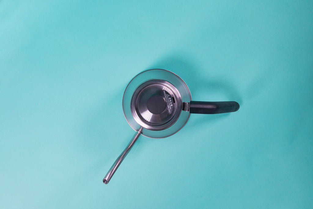 Showing the top of a silver stainless steel kettle with black plastic handle and short cylindrical black plastic lid knob set against a blue background.