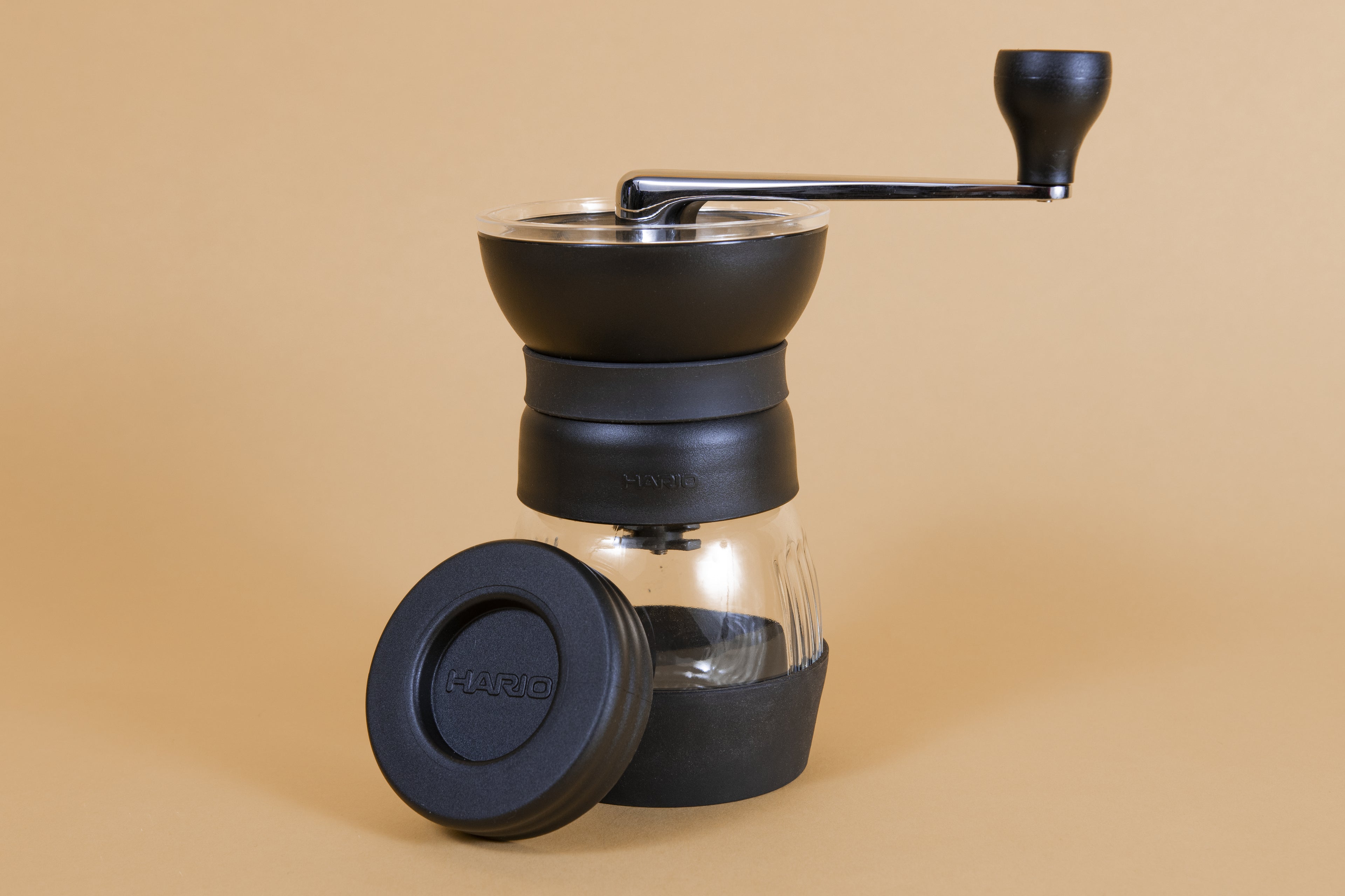 Black plastic coffee mill with handle attached to a glass container via screw top with a rubber base, and plastic lid.