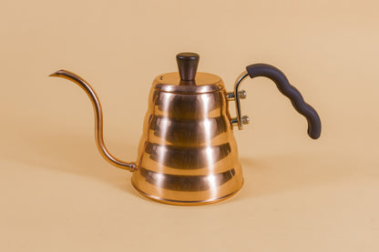 Copper goose neck kettle and matching lid with wood knob and brown rubber covered handle on an orange backdrop.