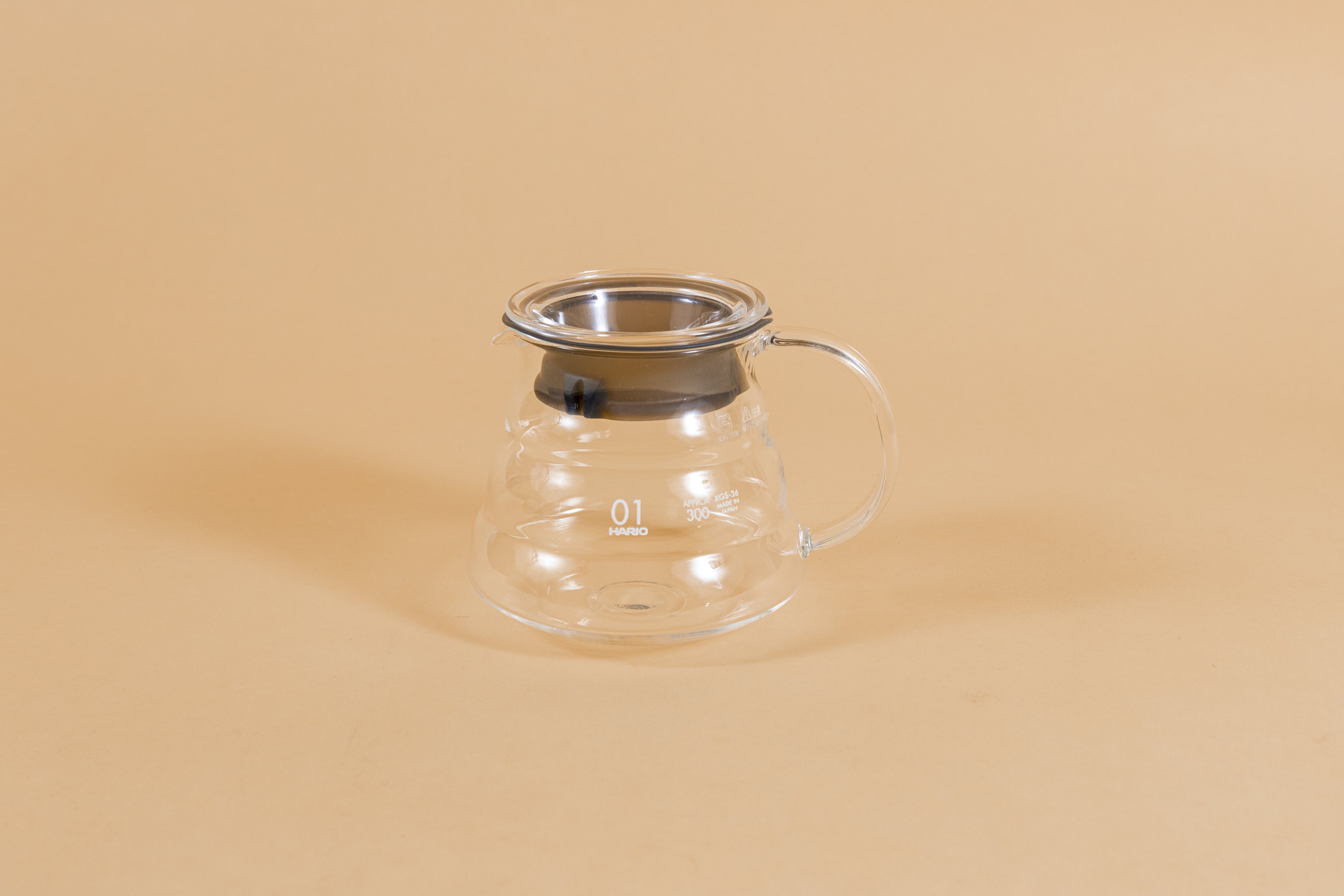 All glass beehive shaped coffee server with handle and glass lid with dark plastic rubber gasket on orange backdrop.