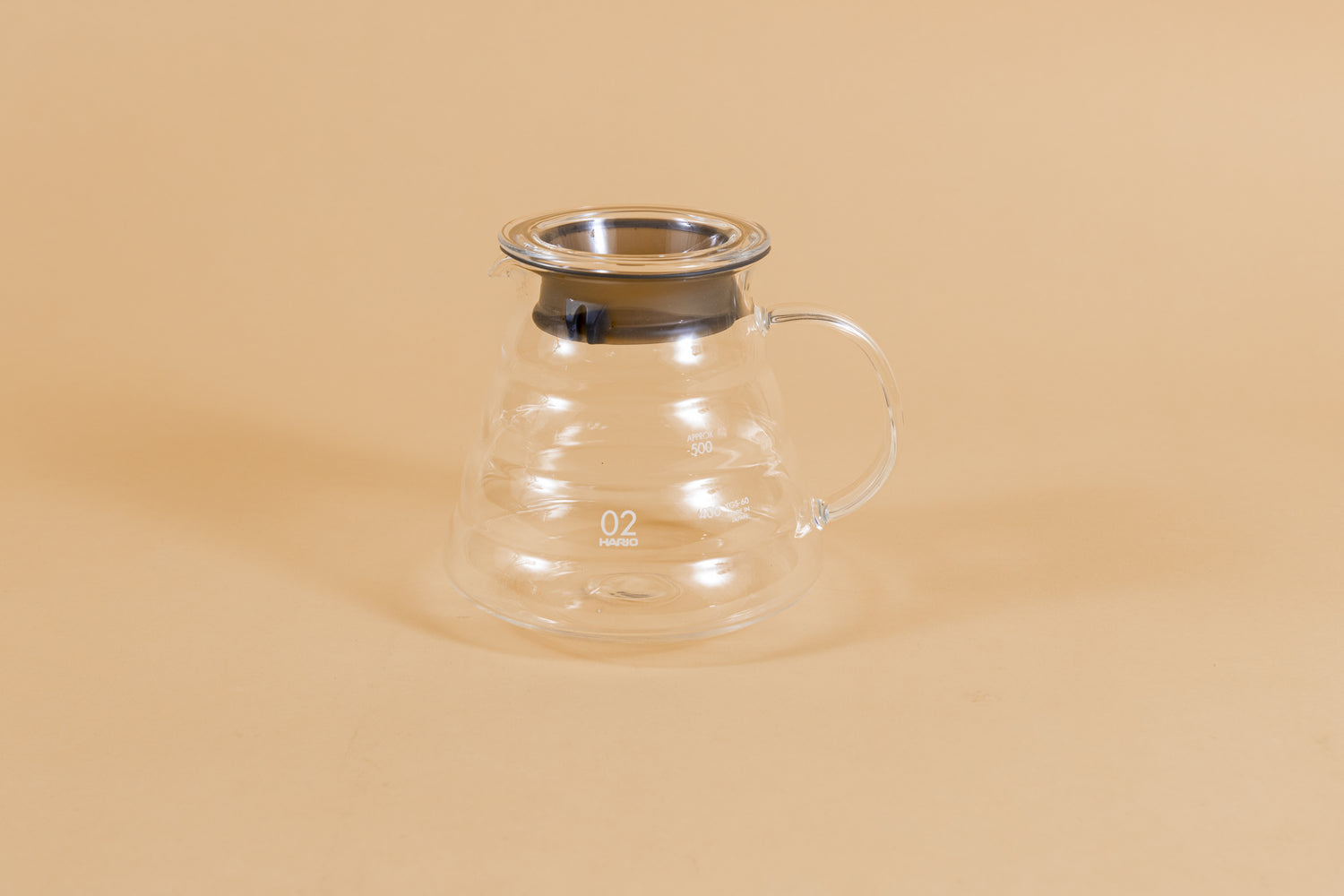 All glass beehive shaped coffee server with handle and glass lid with dark plastic rubber gasket on orange backdrop.