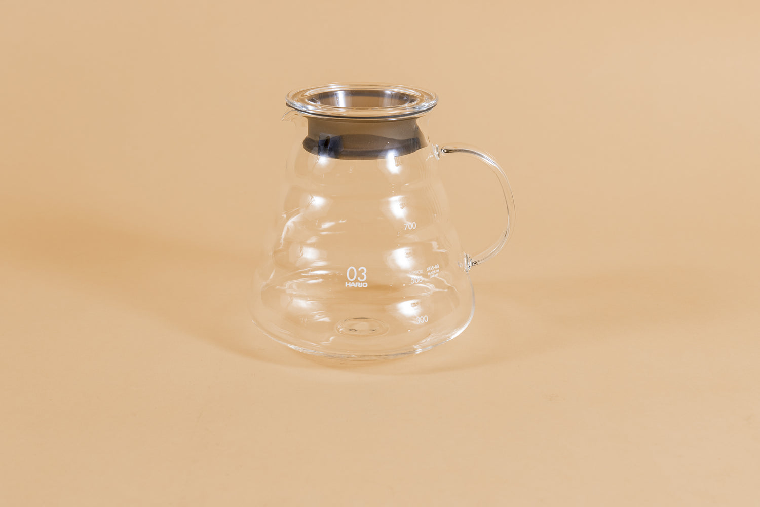 All glass beehive shaped coffee server with handle and glass lid with dark plastic rubber gasket on orange backdrop.