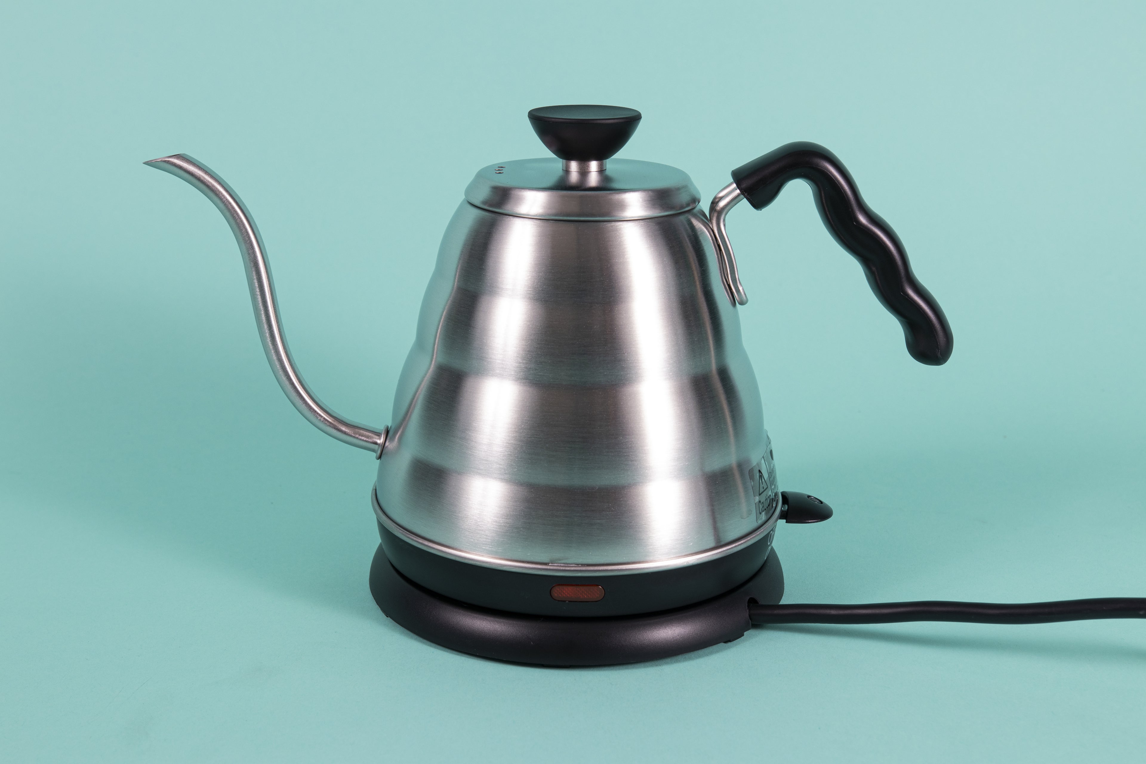 Stainless steel gooseneck kettle and matching lid with plastic base with red LED knob and black plastic covered handle on top a heating base with powercord on a teal backdrop.