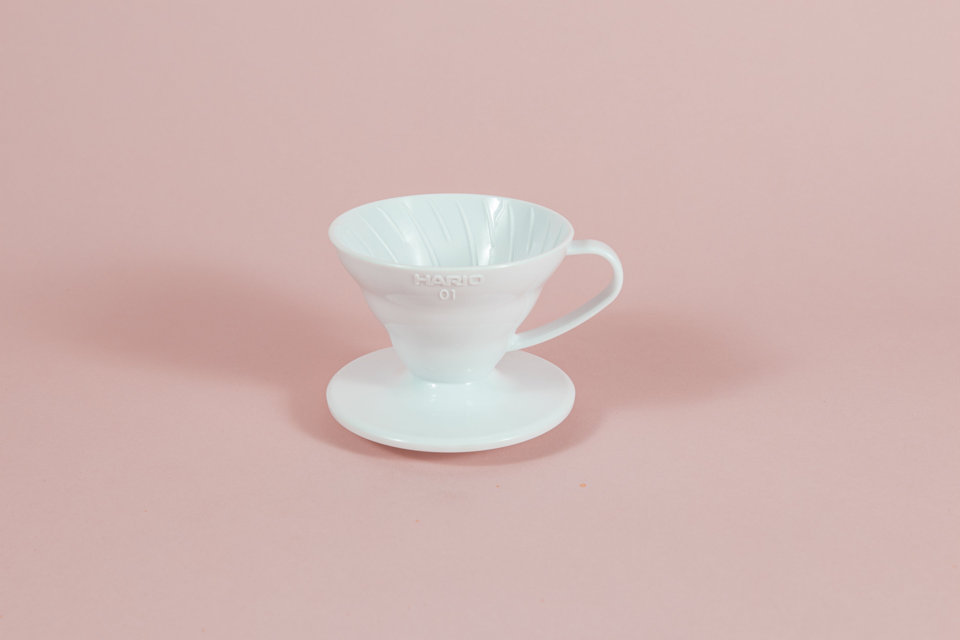 White all plastic cone shaped dripper with handle and round base on a pink backdrop.
