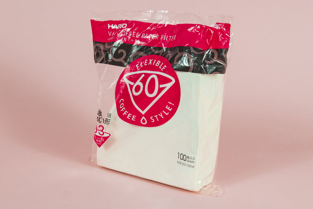 Large pack of white cone filters in plastic packaging with round pink with white text "60" graphic on an orange backdrop.