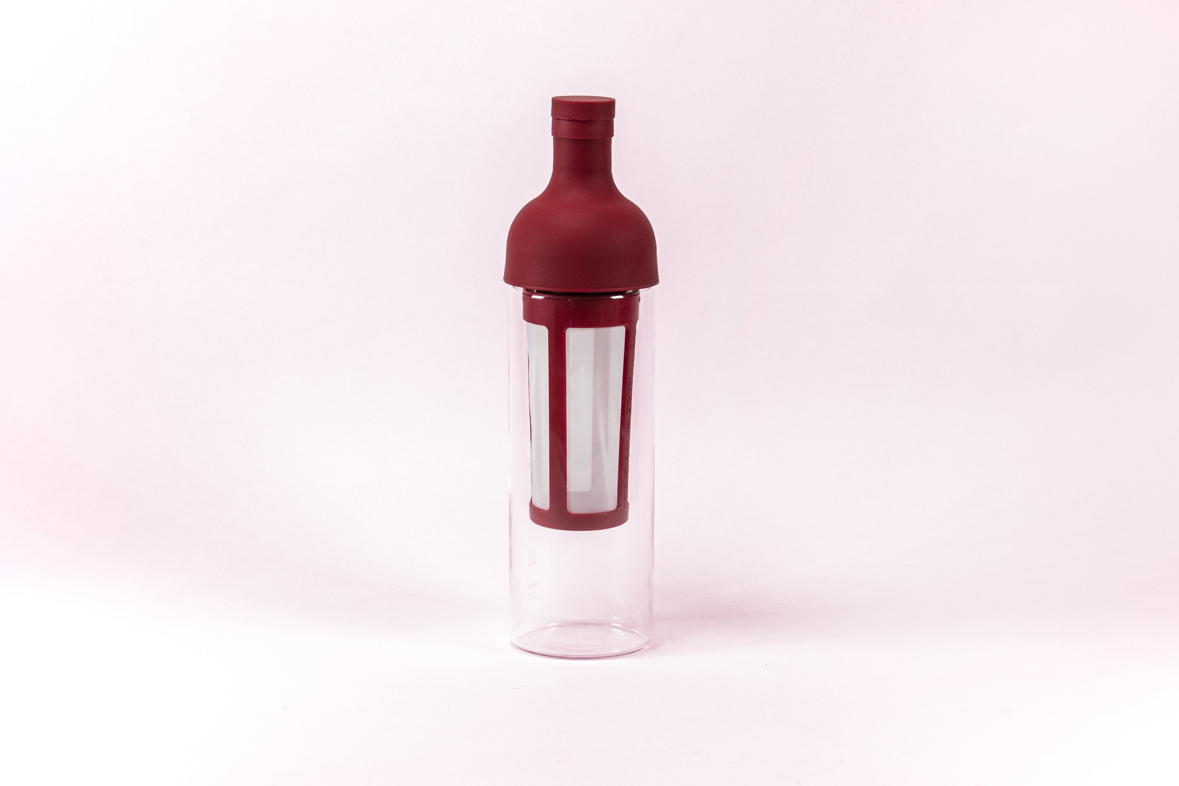 Tall glass container and white nylon mesh coffee filter, with red rubber wine bottle shaped top.