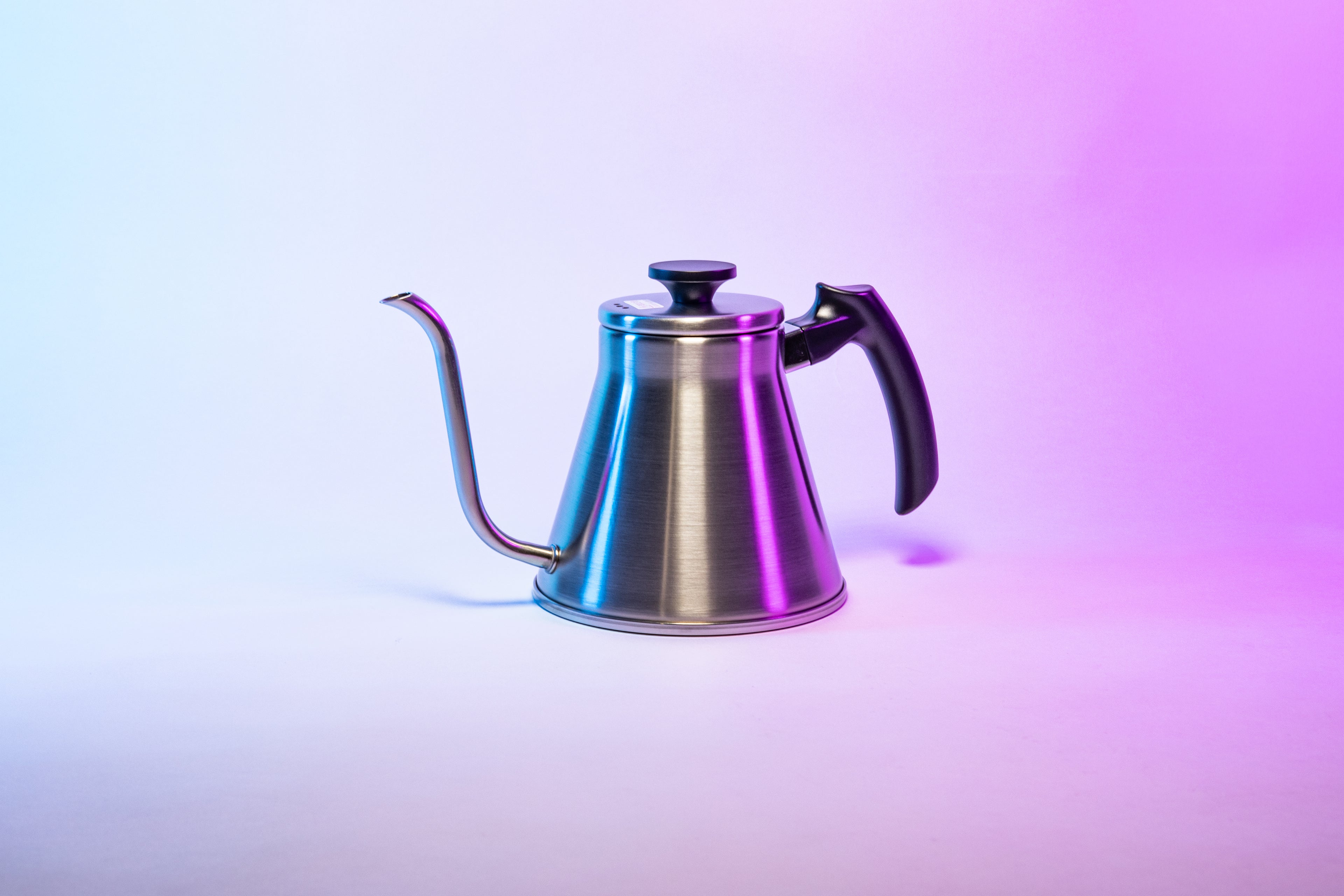 Stainless steel kettle with gooseneck spout, sloped black plastic handle and flat, black plastic lid knob set against a purple gradient background.