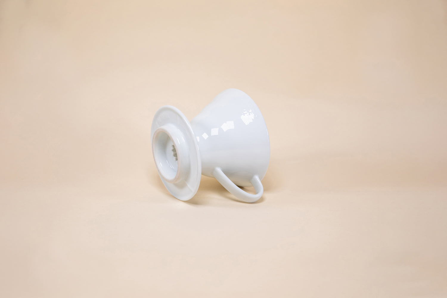 White cone shaped ceramic coffee dripper with handle and round base laying on its side.