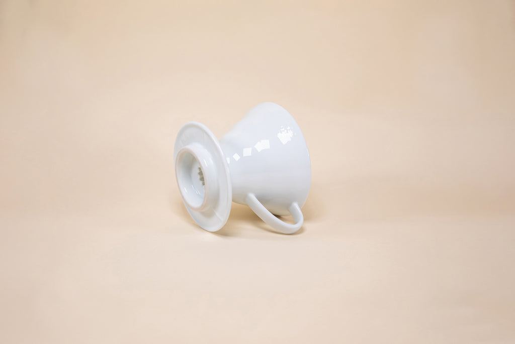 White cone shaped ceramic coffee dripper with handle and round base laying on its side.