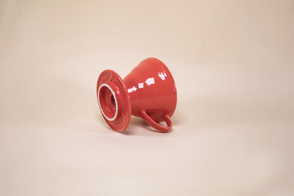 Red cone shaped ceramic coffee dripper with handle and round base laying on its side.