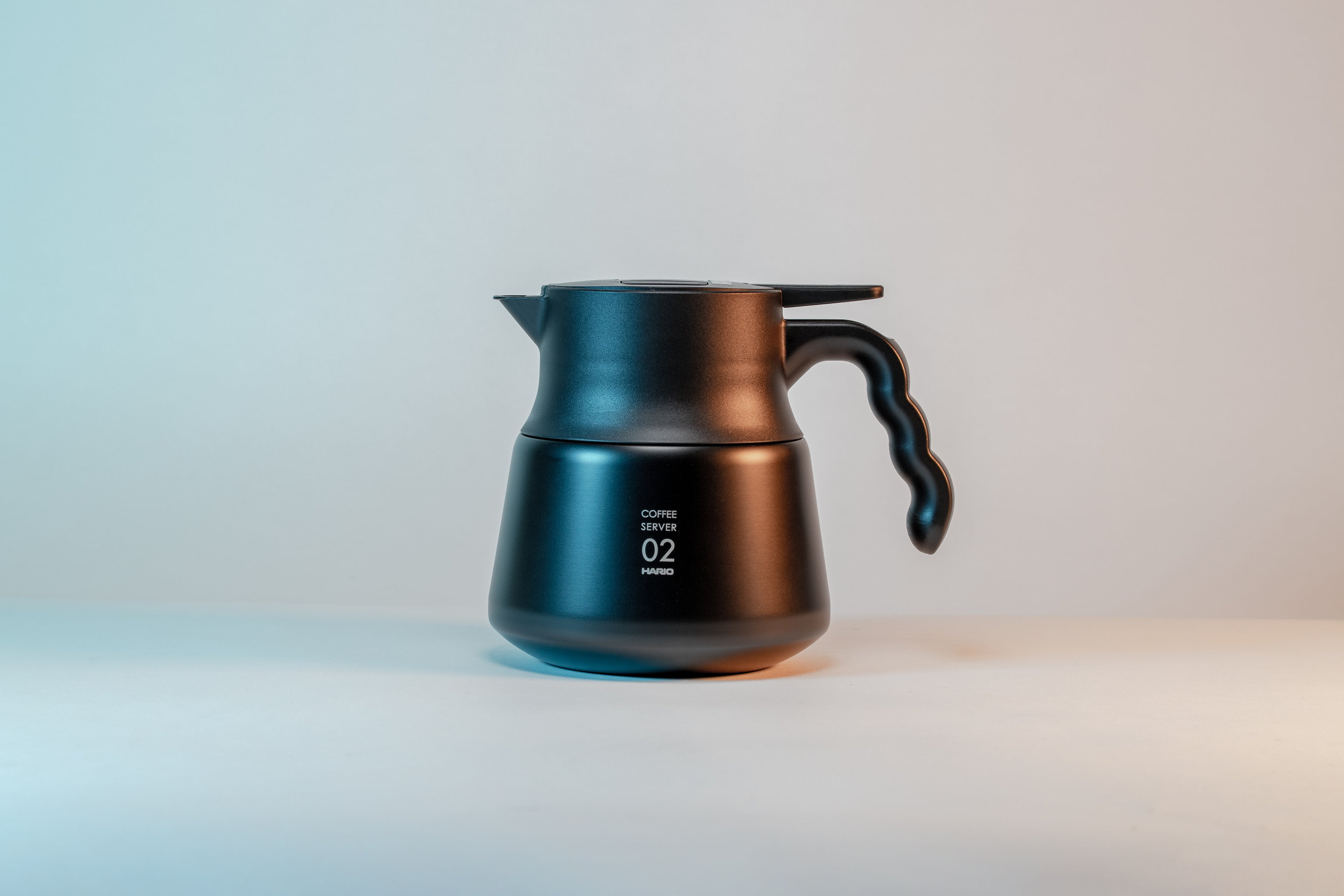 Matte black coffee server with wavy black plastic handle on a light background.