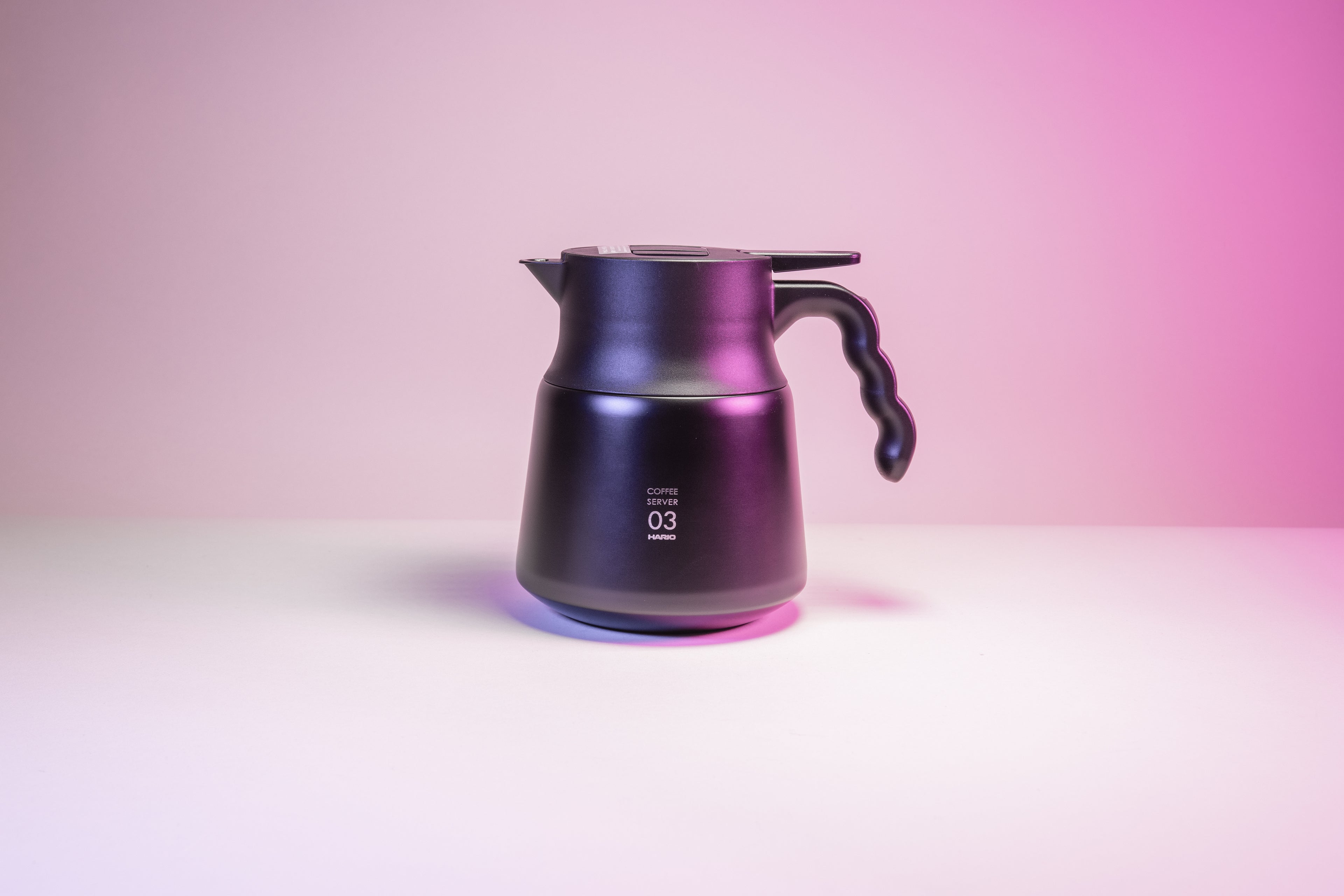 Matte black coffee server with wavy black plastic handle on a pink gradient background.