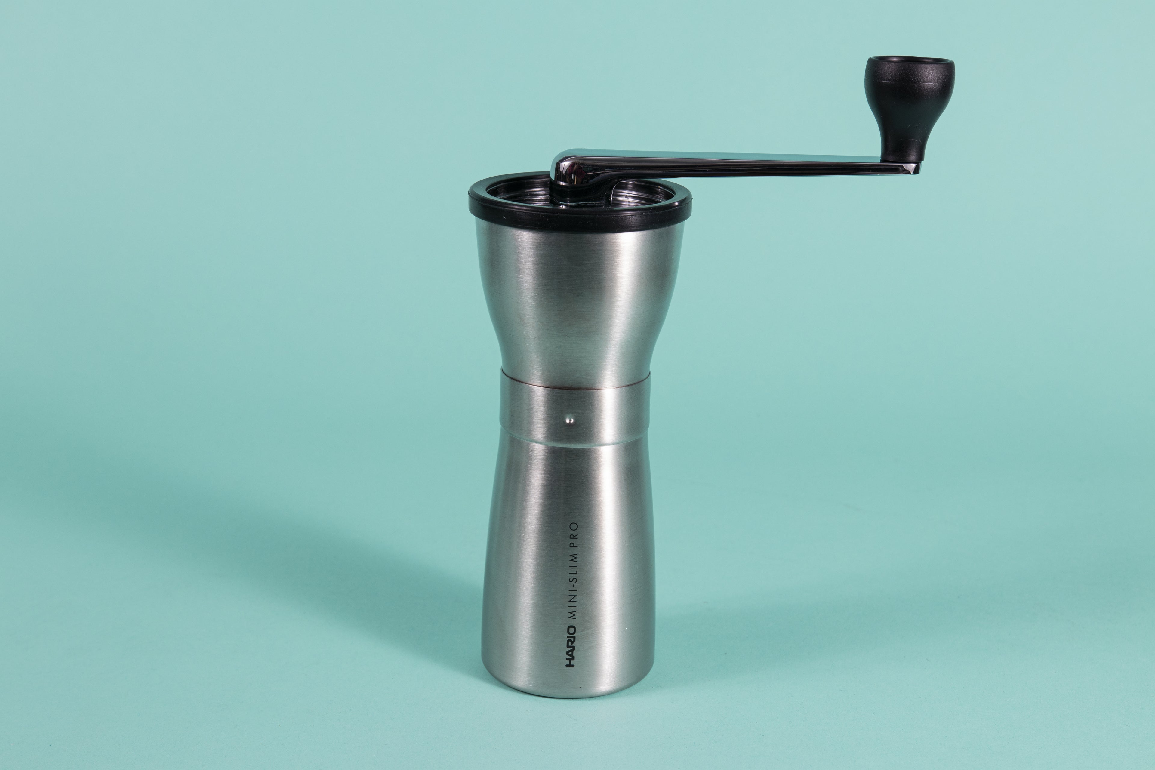 Slim silver metal coffee grinder with rubber lid and metal lever with black plastic knob at the end.